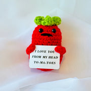 Crocheted Tomato character holding a sign with text on a white background
