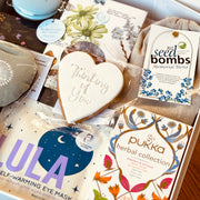 Box containing various items including a heart-shaped cookie, seed bombs, and Pukka herbal collection packaging.