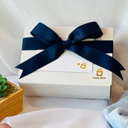 White gift box with a navy blue ribbon on a white surface, featuring the 'Care Box' brand.
