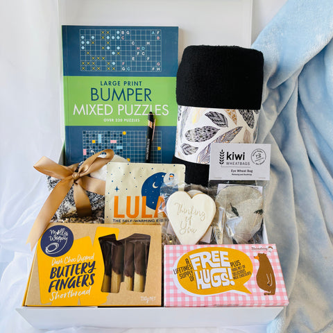 Gift basket with puzzles, snacks, and a blanket on a white background
