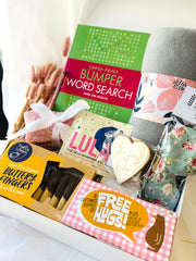 Gift basket with snacks, a book, and a card on a white surface