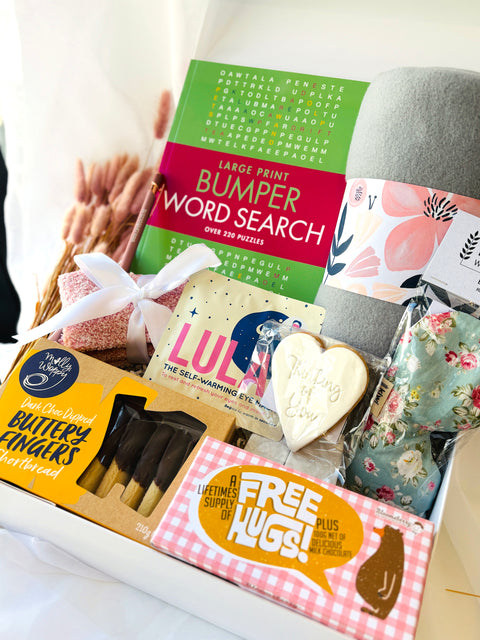 Gift basket with snacks, a book, and a card on a white surface