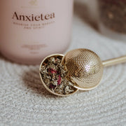 Tea infuser with dried herbs and a 'Anxietae' product in the background