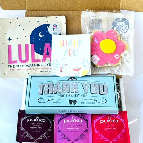 Collection of 'Thank You' items including Chocolate bar, heated eye mask, card, a flower-shaped item, and Pukka tea bags in a box.