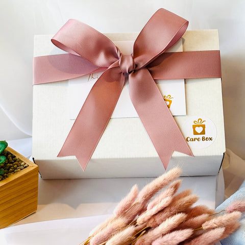 White gift box with a pink ribbon on a white surface with decorative elements.