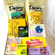 Assorted snacks and products including popcorn bags, eye masks, and bath salts in a box.
