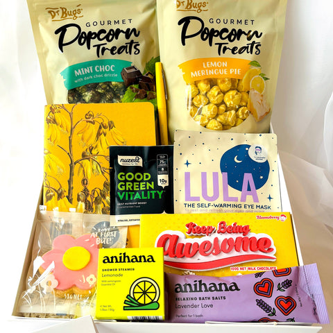 Assorted products including popcorn treats, eye masks, and bath bombs in a box on a white background.